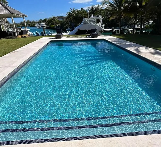 Clear, well maintained rectangular swimming pool with dark waterline tile beside a waterfront property
