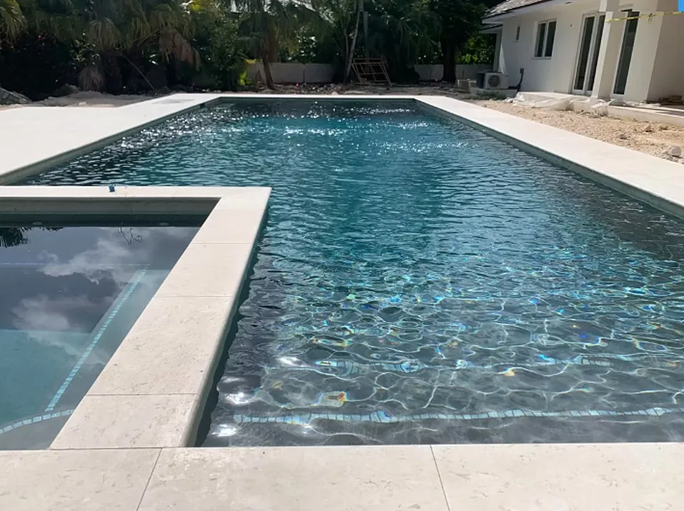 Rectangular swimming pool with a raised spa, dark waterline tile and pale stone coping beside a house