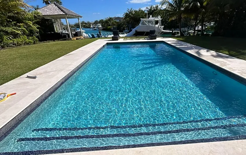 Long rectangular swimming pool with a dark waterline tile band, bordered by lawn and a boat dock beyond