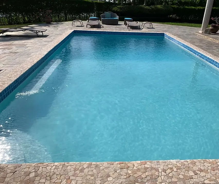 Swimming pool with a shallow sun shelf and wide stone deck, with sun loungers arranged along one side