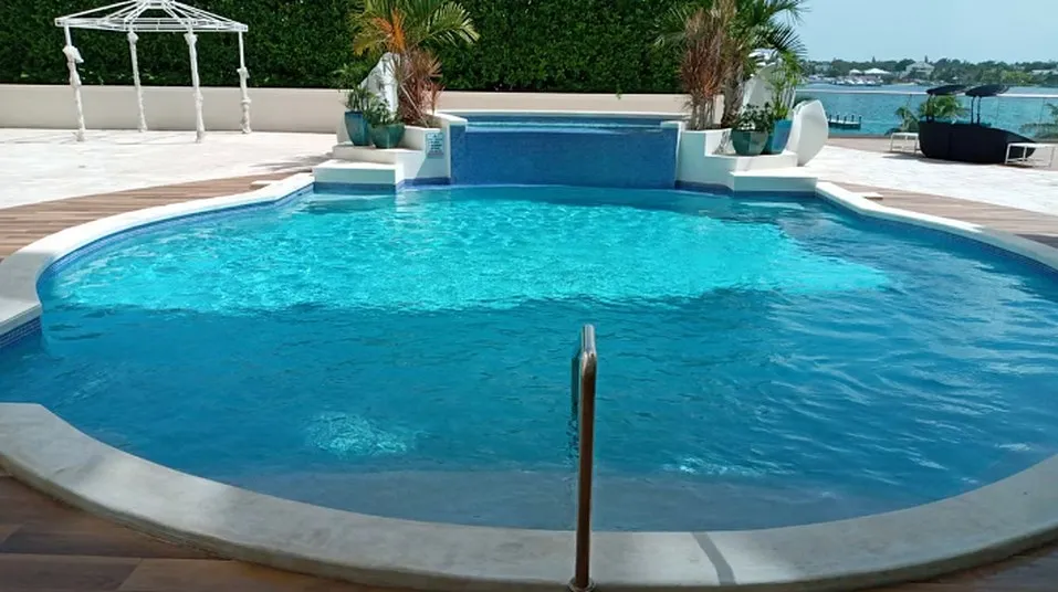 Curved swimming pool with an integrated spa, planters and a white gazebo beside the water