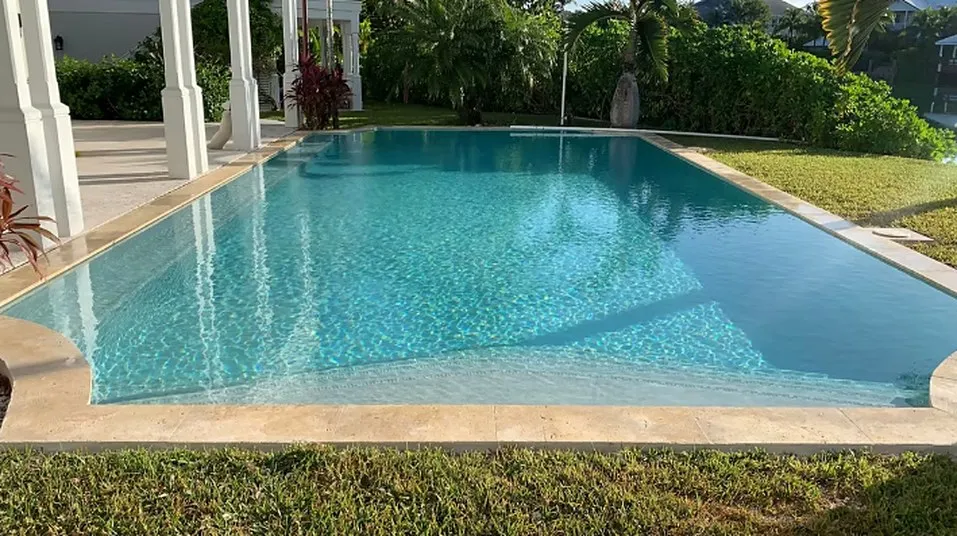 Swimming pool beside a covered patio with white columns, bordered by lawn and garden planting