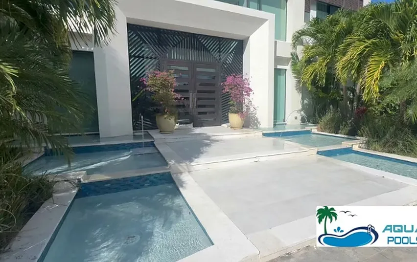 Courtyard swimming pool and spa set into a pale stone deck beside the entrance of a modern home