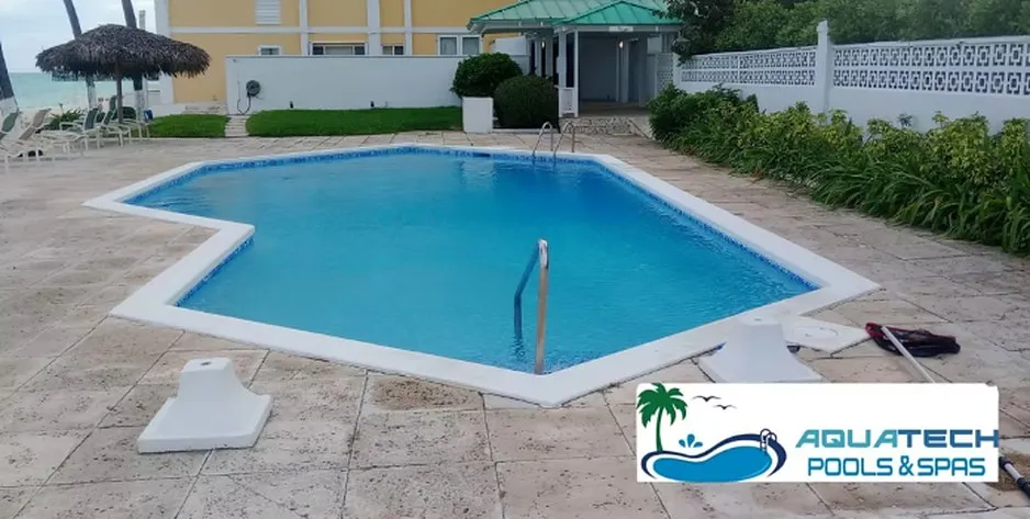 Freeform swimming pool with a paved deck and safety rail beside a residential building
